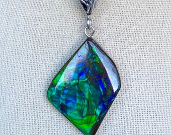 May include: A silver chain necklace with a diamond-shaped pendant featuring a green, blue, and black iridescent opal.