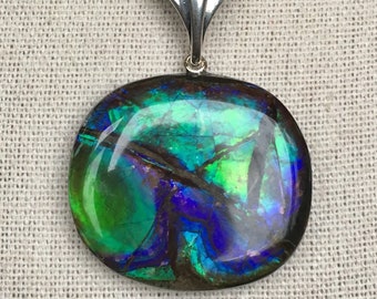 May include: A silver chain necklace with a pendant featuring a large, oval-shaped iridescent opal gemstone with green, blue, and purple hues.
