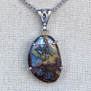 May include: A silver pendant necklace featuring an oval-shaped opal gemstone. The opal displays a mix of colors, including blue, brown, and yellow, with a unique pattern. The pendant is suspended from a delicate silver chain, creating an elegant accessory.
