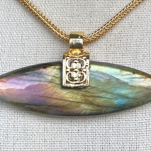 May include: A gold chain necklace with a pendant featuring a large, iridescent labradorite gemstone in a teardrop shape. The pendant has a gold filigree design.