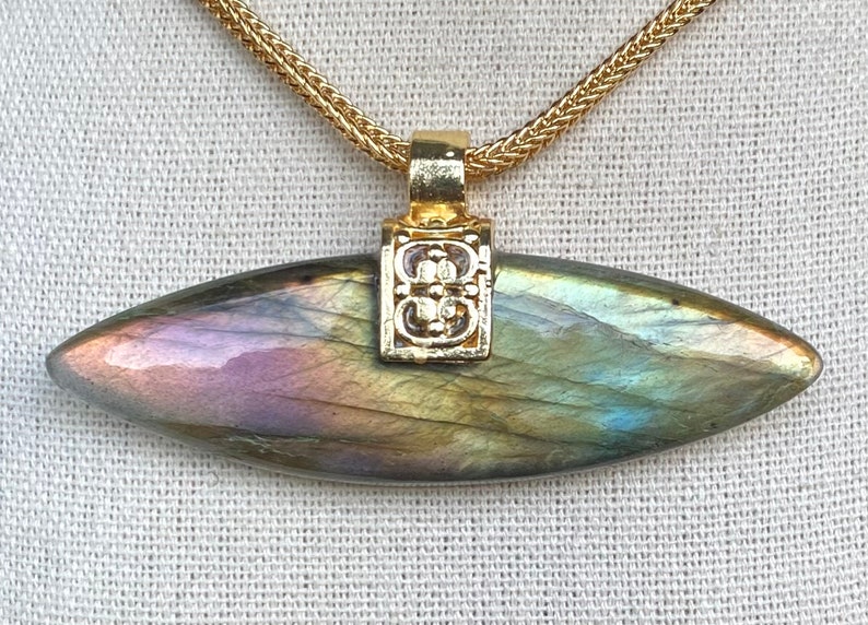 May include: A gold chain necklace with a pendant featuring a large, iridescent labradorite gemstone in a teardrop shape. The pendant has a gold filigree design.