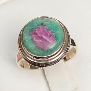 May include: A silver ring with a green and pink gemstone set in a bezel setting. The ring has a double band.