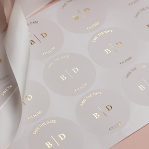 Vergoldete Save The Date Hochzeitssticker mit personalisierten Initialen und Datum. Goldfolienetiketten auf halb durchsichtigem Etikett.