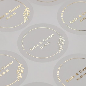 Foiled Save The Date Hochzeitsumschläge Aufkleber mit personalisierten Namen und Datum. Goldlaubkranzetiketten auf halb durchsichtigem Etikett.