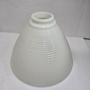 May include: A conical white milk glass lamp shade featuring a textured grid pattern across its surface. The shade has a circular opening at the top with a raised rim, tapering outward toward a wider base, designed for a standard light fixture.