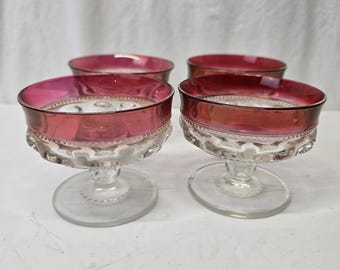 May include: Set of four clear glass stemmed dessert cups with a ruby red rim. The cups have a textured design.