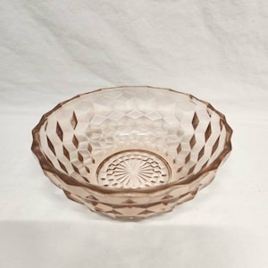 May include: A small, pink glass bowl with a diamond pattern. The bowl is empty and has a smooth, shiny surface.