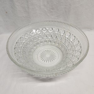 May include: A clear glass bowl with a decorative, raised pattern of circles and lines. The bowl is round and has a wide, shallow shape.