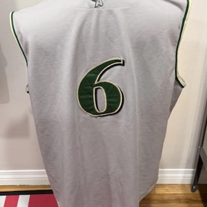 Op de afbeelding: Grijs mouwloos shirt met het nummer 6 in groen en wit. Het shirt heeft groene biezen en een logo op de bovenrug. Het shirt wordt op een mannequin getoond.