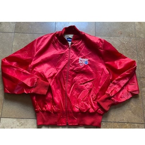 May include: A red satin bomber jacket with a blue and white embroidered logo that says "Hungry Jack's".