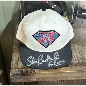 May include: A white and black baseball cap featuring the NFL 75th anniversary logo. The cap has a black brim and the signature "Steve Bartkowski Falcons" in white script.