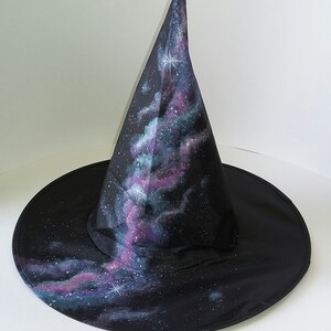 May include: A black witch hat with a pointed crown, painted with a galaxy design featuring swirling clouds of purple, blue, and green, and white stars.
