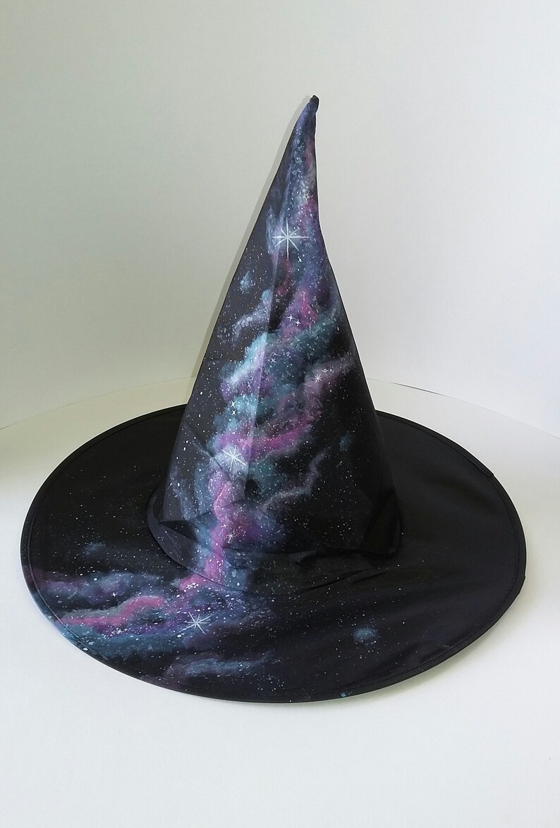 May include: A black witch hat with a pointed crown, painted with a galaxy design featuring swirling clouds of purple, blue, and green, and white stars.