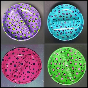 May include: Four ceramic ashtrays with a leopard print design. Each ashtray is a different color: purple, blue, pink, and green.