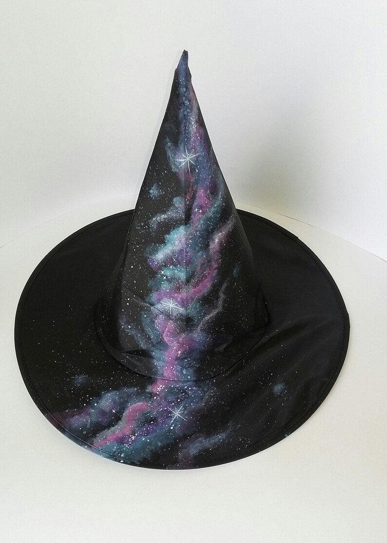 May include: A black witch hat with a galaxy print. The hat has a pointed cone and a wide brim. The galaxy print features shades of blue, purple, and pink with white stars.