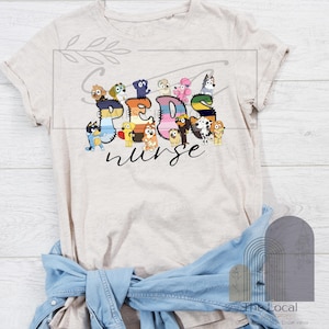 May include: A beige t-shirt with the words "Peds nurse" in a colourful design, incorporating cartoon dog characters. The shirt has short sleeves and a crew neck, with a denim jacket tied around the waist.