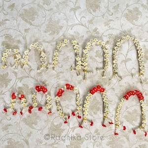 Puede incluir: Un conjunto de nueve guirnaldas de flores blancas con detalles rojos. Las guirnaldas están hechas de flores artificiales y están dispuestas en fila sobre un fondo blanco.