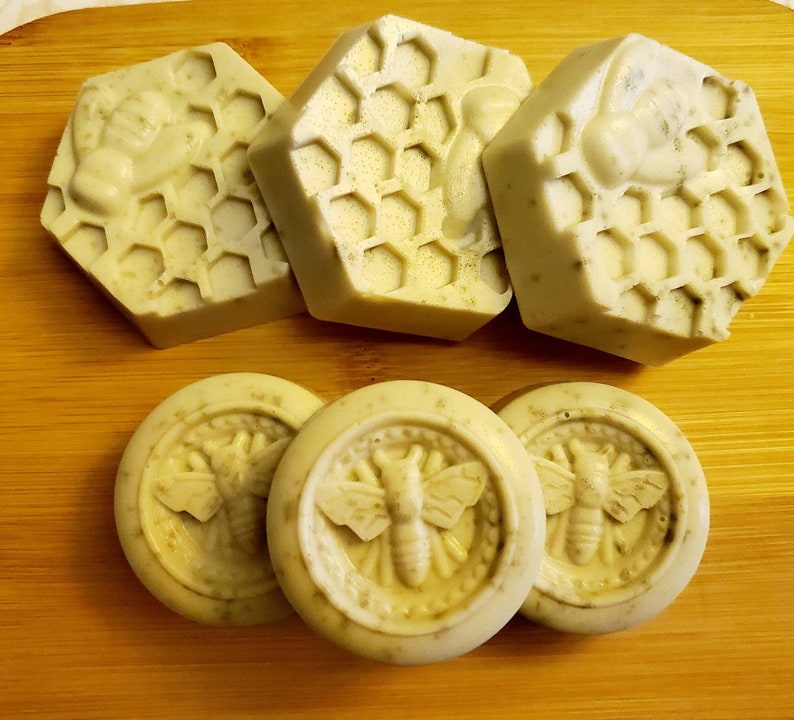 May include: Five handmade soap bars with a honeycomb design and a bee image. The soap bars are on a wooden surface.
