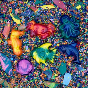 May include: A set of colorful crayon sculptures depicting various sea creatures, including a crab, a seahorse, a fish, an octopus, and a whale. The sculptures are arranged on a bed of colorful crayon shavings.