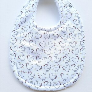 May include: White baby bib featuring a repeating pattern of cartoon chickens in black outline with red combs. The bib has a soft, white terry cloth border. Designed to catch spills and drool.