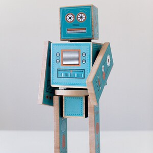 May include: A teal blue wooden robot toy with a printed face, buttons, and dials. The robot has movable arms and legs.