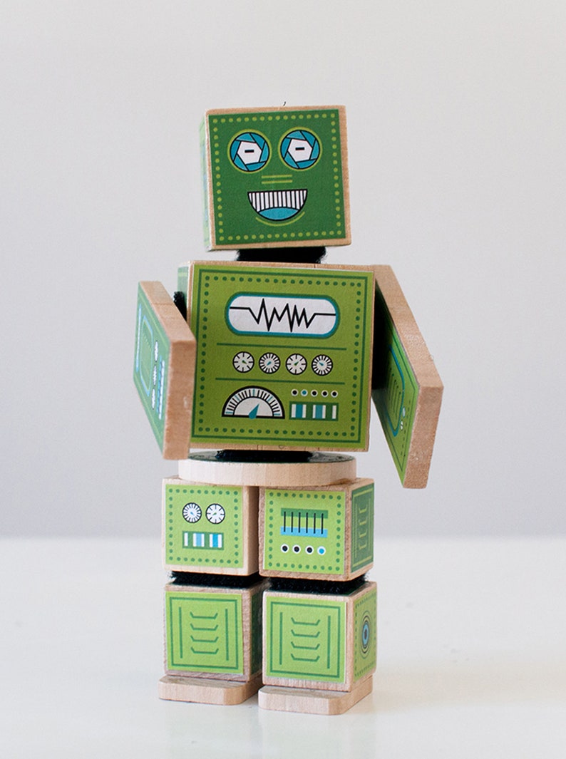 May include: A green wooden robot toy with a smiling face, blue eyes, and a control panel on its chest. The robot has movable arms and legs.