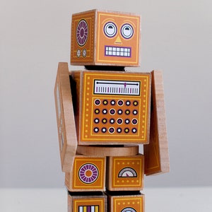 May include: A wooden toy robot with a yellow and orange body, purple and white details, and a smiling face. The robot has a dial, a gauge, and a series of circles on its body.