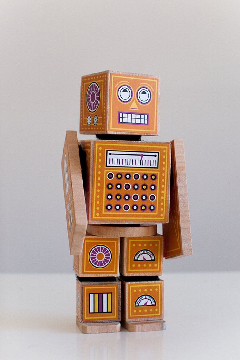 May include: A wooden toy robot with a yellow and orange body, purple and white details, and a smiling face. The robot has a dial, a gauge, and a series of circles on its body.