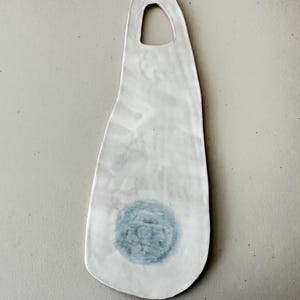 May include: White ceramic serving tray with a blue circle design and a cut-out handle. The tray has an irregular shape and a textured surface.