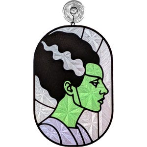 May include: A stained glass window featuring the Bride of Frankenstein in profile. The image has a black outline, with a green face and black hair. The background is silver and the window is oval-shaped.