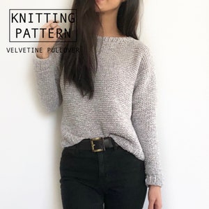 Può includere: Un maglione Velveteen grigio chiaro e strutturato con maniche lunghe. Il maglione è abbinato a pantaloni neri e una cintura nera con fibbia dorata. L'immagine include il testo "KNITTING PATTERN" e "VELVETINE PULLOVER".