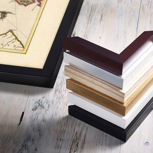 May include: A stack of picture frames in various colors, including black, white, brown, and gold. The frames are made of wood and have a simple, classic design.