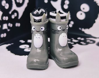 May include: A pair of gray rain boots with white and black striped socks. The boots have a cartoon character face on the front. The background is a black and white pattern.
