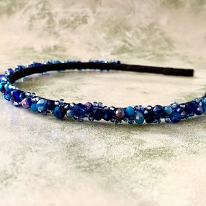 May include: A blue beaded headband with a black elastic band. The headband is decorated with small, iridescent blue beads.