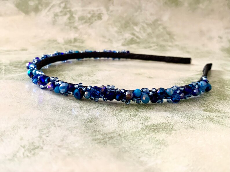 May include: A blue beaded headband with a black elastic band. The headband is decorated with small, iridescent blue beads.