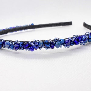 May include: A blue beaded headband with a black elastic band. The headband is decorated with blue and dark blue beads.