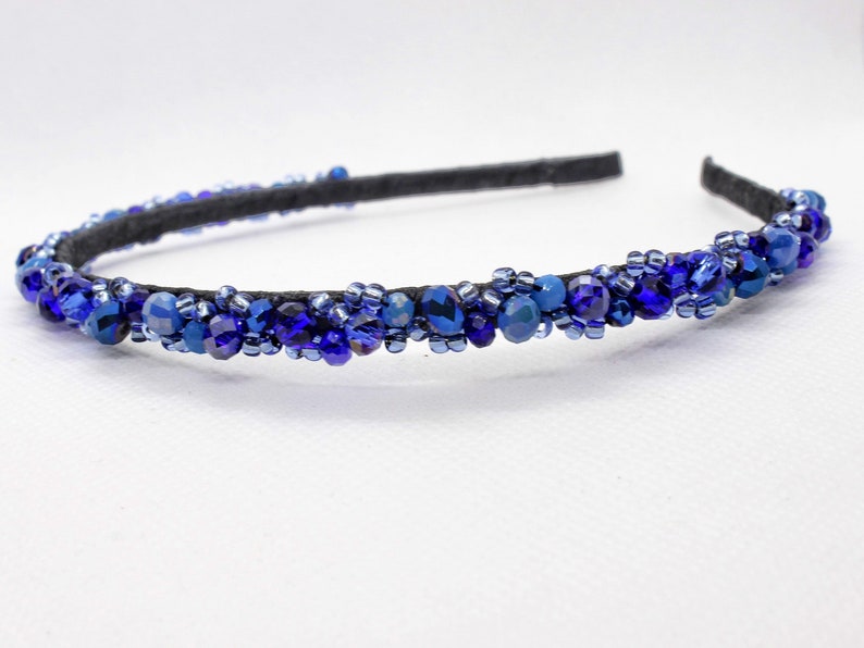 May include: A blue beaded headband with a black elastic band. The headband is decorated with blue and dark blue beads.
