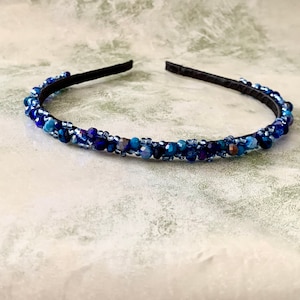 May include: A blue beaded headband with a black elastic band. The headband is decorated with blue and purple beads.