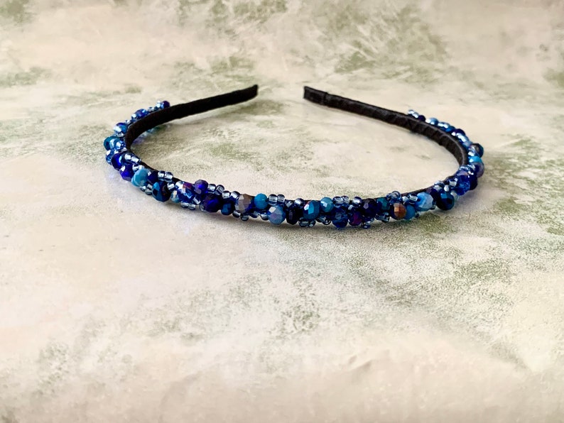 May include: A blue beaded headband with a black elastic band. The headband is decorated with blue and purple beads.