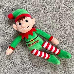 May include: A plush elf doll with a green outfit, red collar, and a matching hat with a red pom-pom. The elf's legs are striped red and white. The name "Ronnie" is embroidered on the doll's torso.