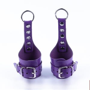 May include: A pair of purple leather wrist cuffs with silver metal rings and buckles. The cuffs have a loop at the top for hanging.