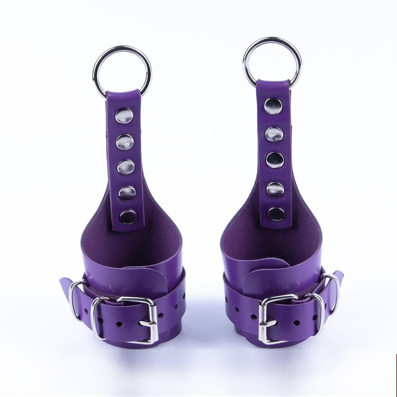 May include: A pair of purple leather wrist cuffs with silver metal rings and buckles. The cuffs have a loop at the top for hanging.