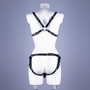 May include: Black leather body harness with adjustable straps and metal hardware. The harness has a crisscross design on the back and a separate piece around the hips. The product is displayed on a white mannequin.