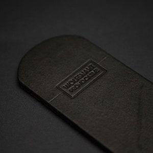 May include: A black leather item with rounded edges, featuring the embossed text "WOLFSNAKE PROVOCATIVE" in a rectangular frame. The item has a textured surface and a dark background.