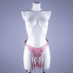 May include: Pink leather harness with silver metal rings and chains. The harness has a belt with two buckles and a strap that goes between the legs.