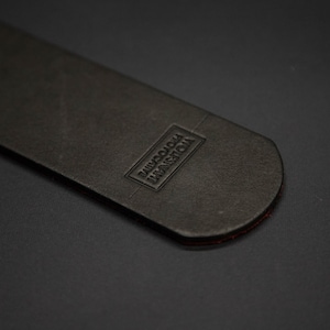 May include: A close-up of a black leather item with a rectangular embossed label that reads "VIOLENT PHOTOCRIME". The item has a rounded end with a thin red edge.