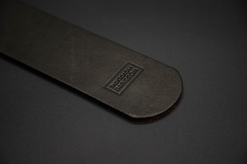 May include: A close-up of a black leather item with a rectangular embossed label that reads "VIOLENT PHOTOCRIME". The item has a rounded end with a thin red edge.