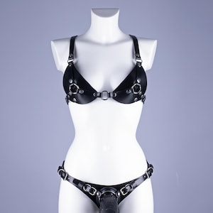 May include: Black leather lingerie set comprising a bra and matching bottom. The bra has adjustable straps and metal ring accents. The bottom features a similar design with a metal ring and a waist strap.