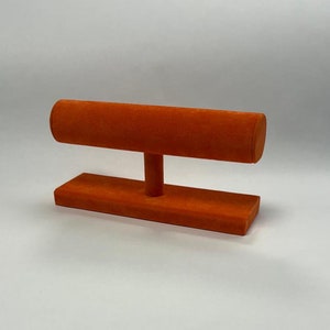 May include: Orange velvet jewellery stand with a cylindrical top for displaying bracelets.