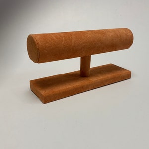 May include: A brown suede bracelet display stand with a round top and a rectangular base.